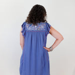Woman wearing a blue dress with floral embroidery on a white background