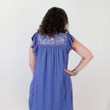 Woman wearing a blue dress with floral embroidery on a white background