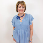 Woman wearing a light blue blouse with a blue ribbon and necklace against a white background