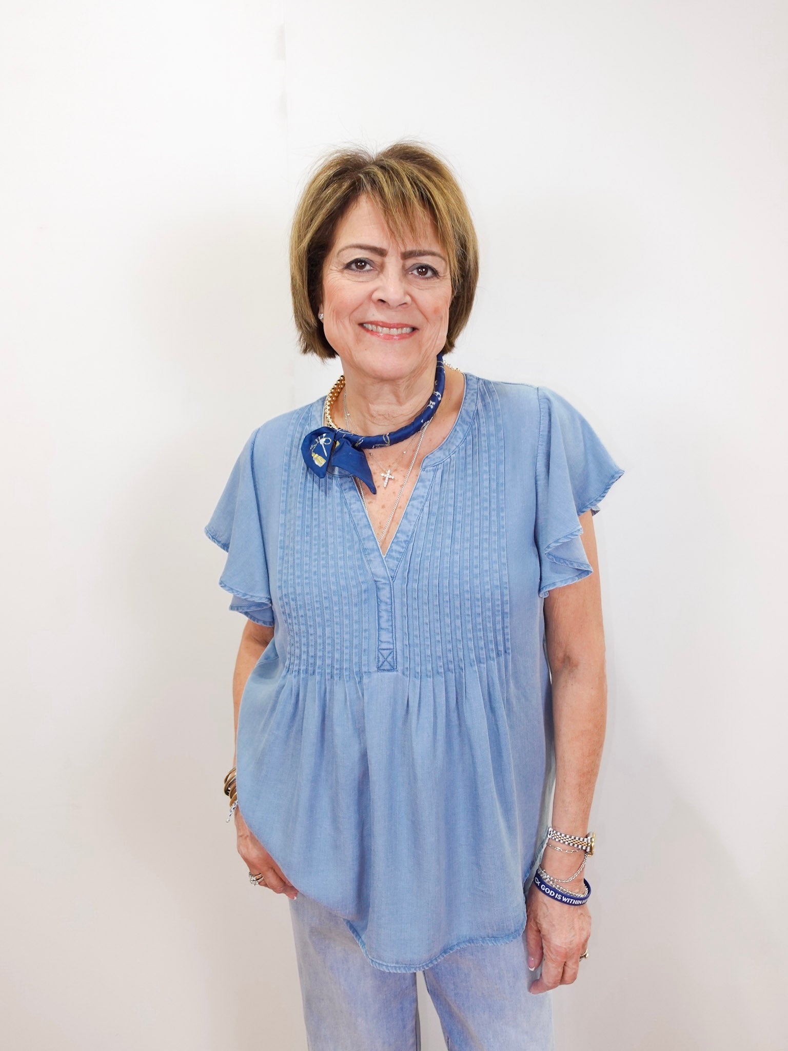 Woman wearing a light blue blouse with a blue ribbon and necklace against a white background