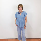 Woman wearing a blue outfit with white sneakers against a white wall.