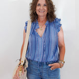 Woman wearing a blue striped sleeveless top and jeans, holding a beige bag against a white background