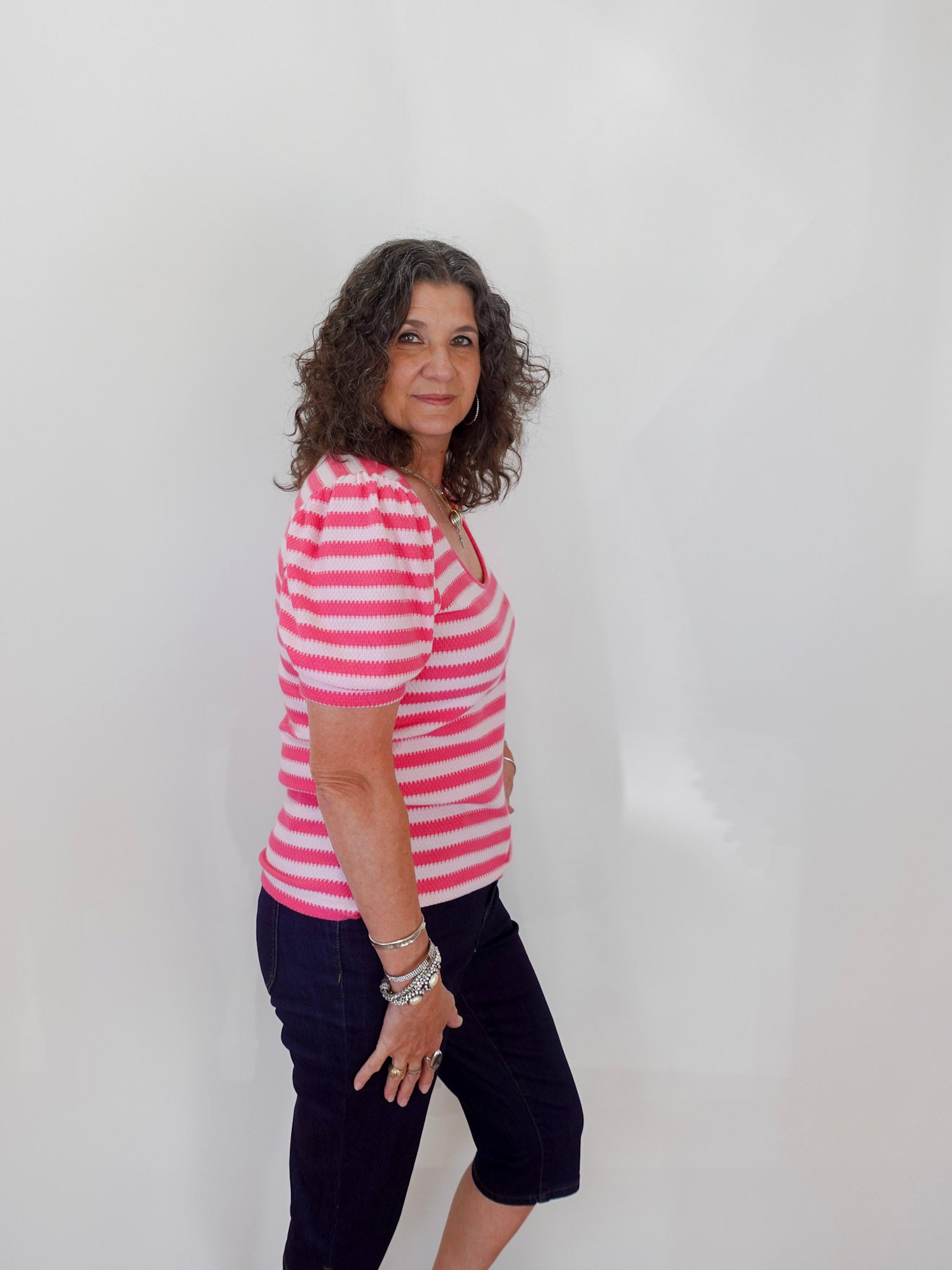 Woman wearing a pink and white striped shirt and black pants against a white background