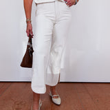Person wearing a white outfit with a brown handbag on a plain background