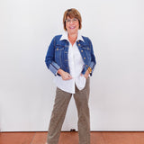 Woman wearing a denim jacket, white shirt, and patterned pants against a white wall.