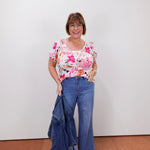 Woman wearing a floral top and blue jeans against a white wall.