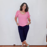 Woman wearing a pink and white striped shirt, navy blue pants, and green sneakers against a white wall.