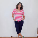 Woman wearing a pink and white striped shirt, navy blue pants, and green sneakers against a white wall.