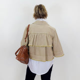 Person wearing a beige jacket with fringe details, holding a brown bag against a white background