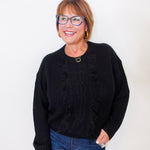 Woman wearing a black sweater and blue jeans against a white background
