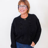 Woman wearing a black sweater and blue jeans against a white background
