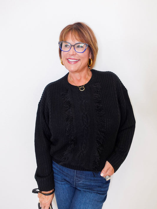 Woman wearing a black sweater and blue jeans against a white background