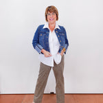 Woman wearing a denim jacket, white shirt, and patterned pants against a white wall.