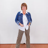 Woman wearing a denim jacket, white shirt, and patterned pants against a white wall.