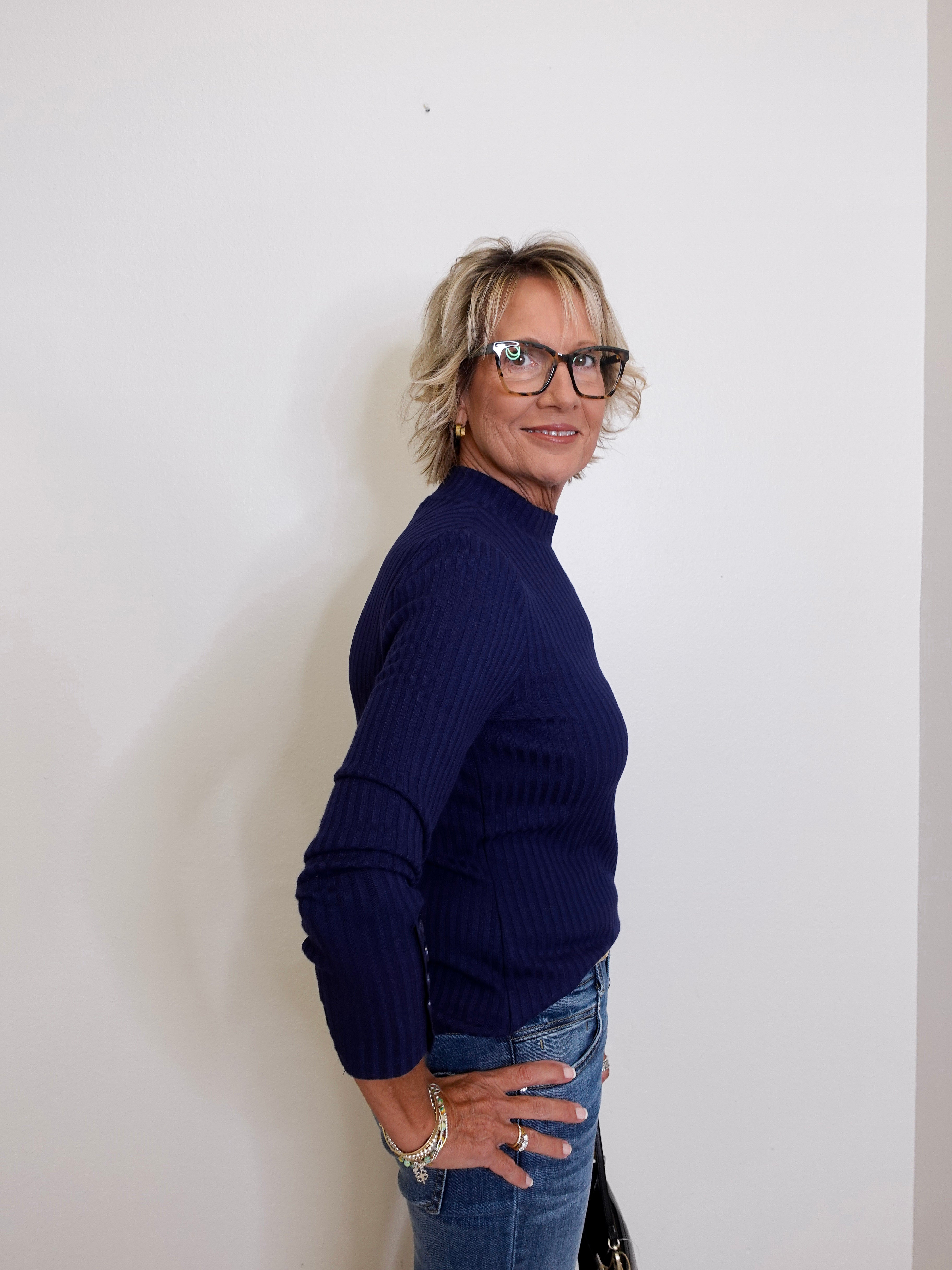 Woman wearing a navy sweater and jeans against a white wall