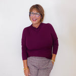 Woman wearing a purple sweater and patterned pants against a white background