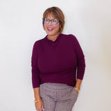 Woman wearing a purple sweater and patterned pants against a white background