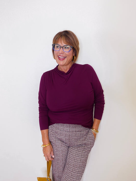 Woman wearing a purple sweater and patterned pants against a white background