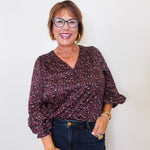 Woman wearing a patterned blouse and jeans against a plain background