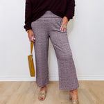 Person wearing a dark burgundy top and plaid pants standing against a white wall.