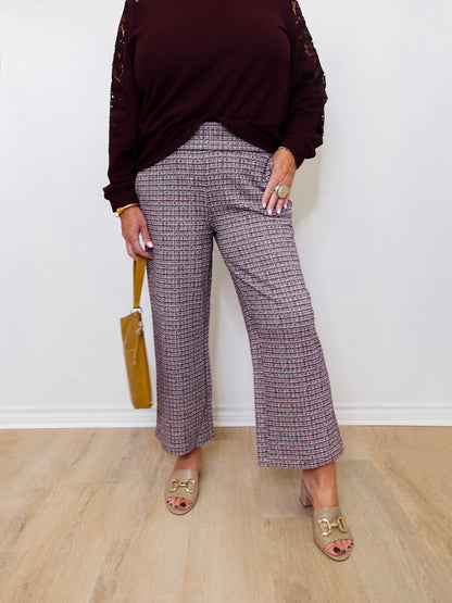 Person wearing a dark burgundy top and plaid pants standing against a white wall.