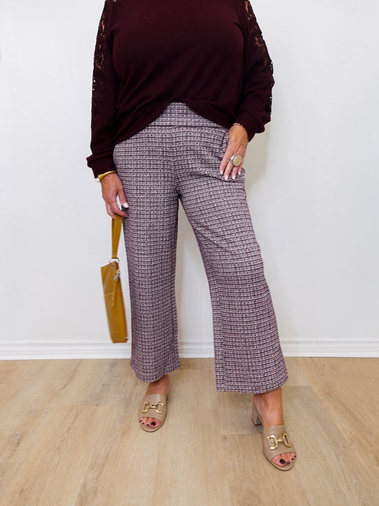 Person wearing a dark burgundy top and plaid pants standing against a white wall.