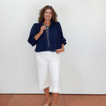 Woman wearing a navy blue top and white pants standing against a plain white wall.