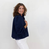 Woman wearing a navy blue top and white pants against a plain background