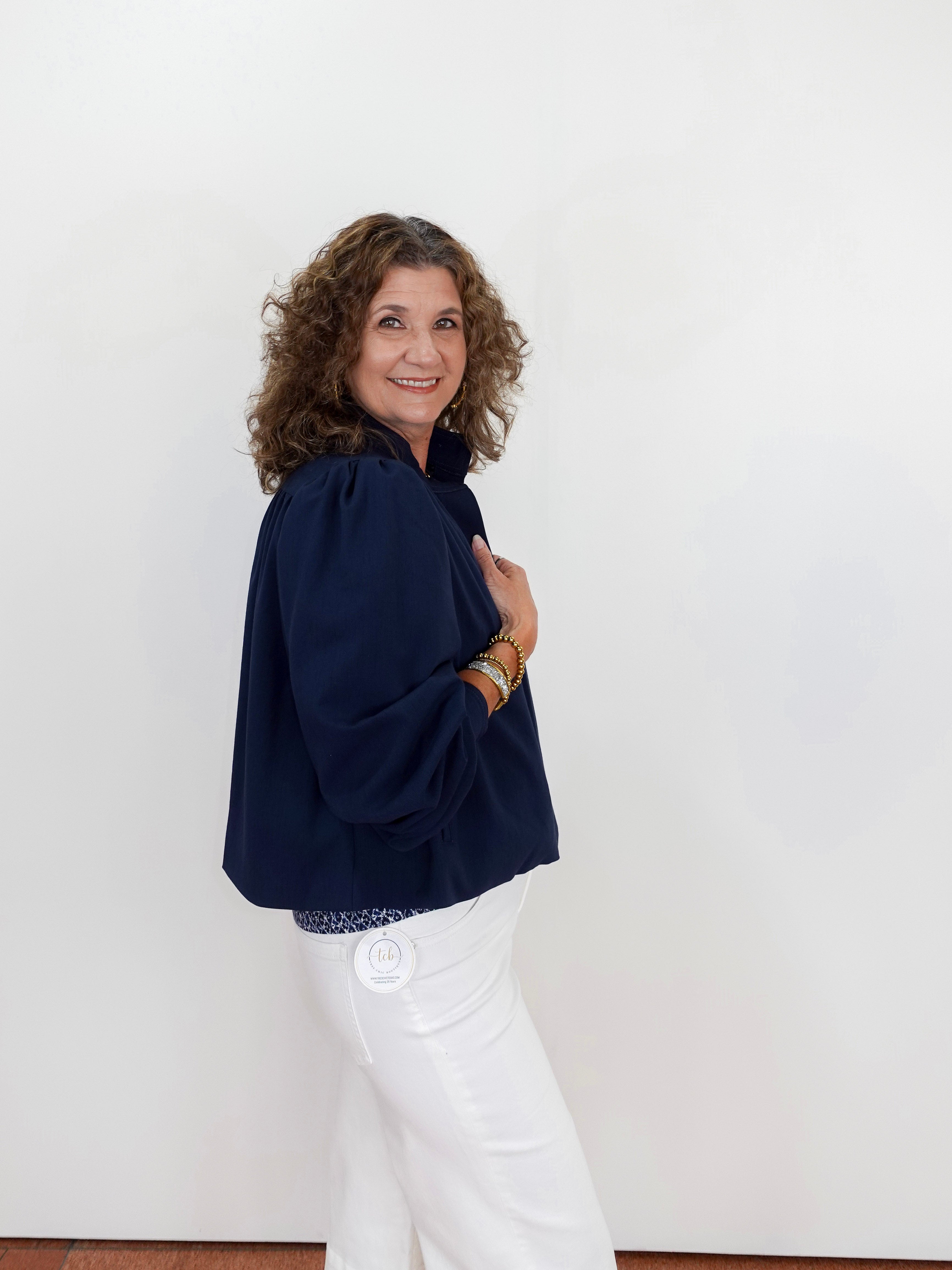 Woman wearing a navy blue top and white pants against a plain background