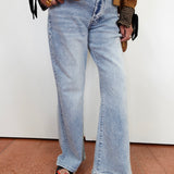 A person wearing light-wash wide-leg denim jeans, styled with a brown jacket, striped top, and black slide sandals with red nail polish, standing against a plain white wall.