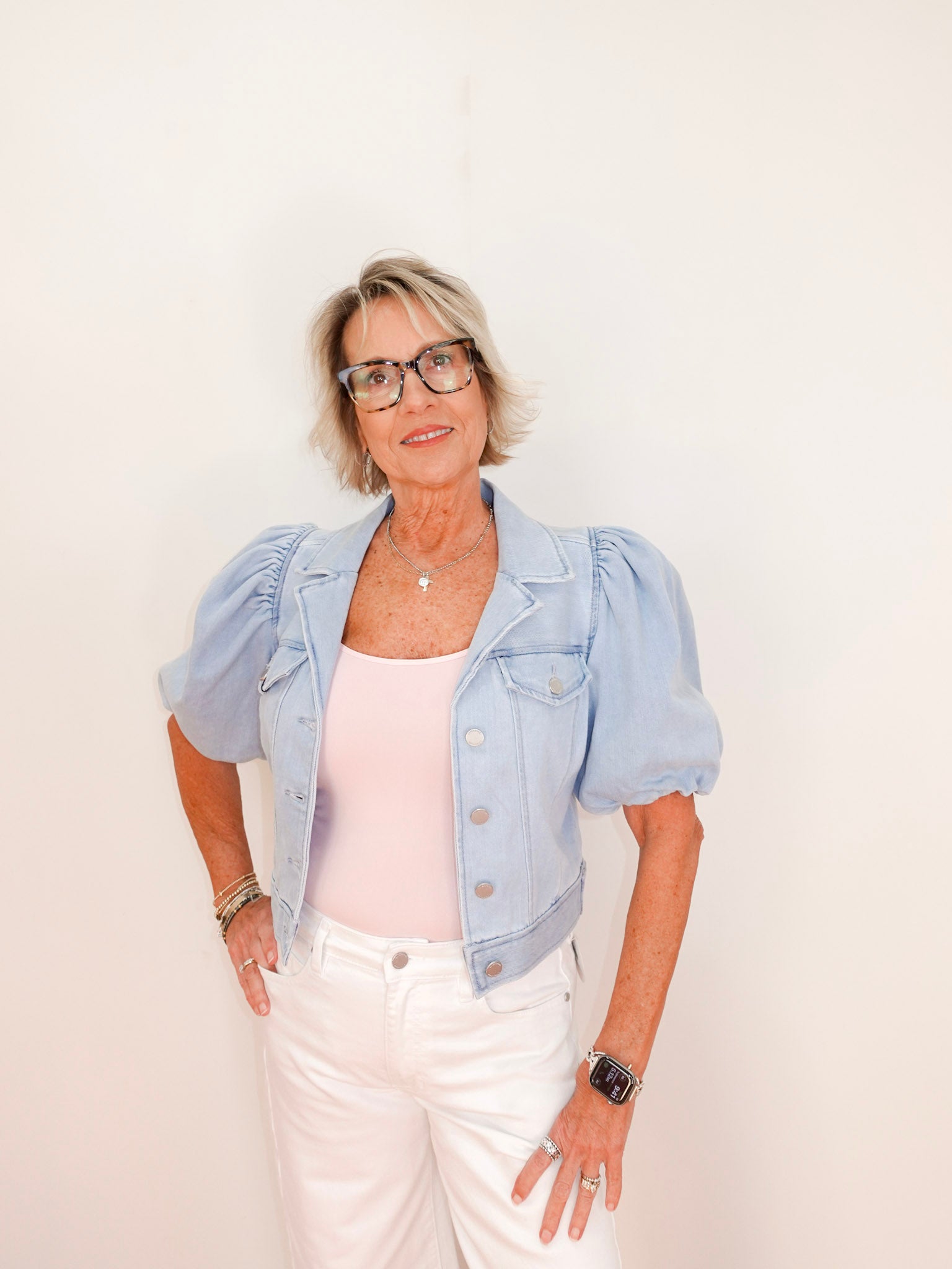 Woman wearing a light blue denim jacket over a white top and pants on a plain background