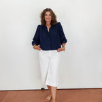 Woman wearing a navy blouse and white pants against a plain background