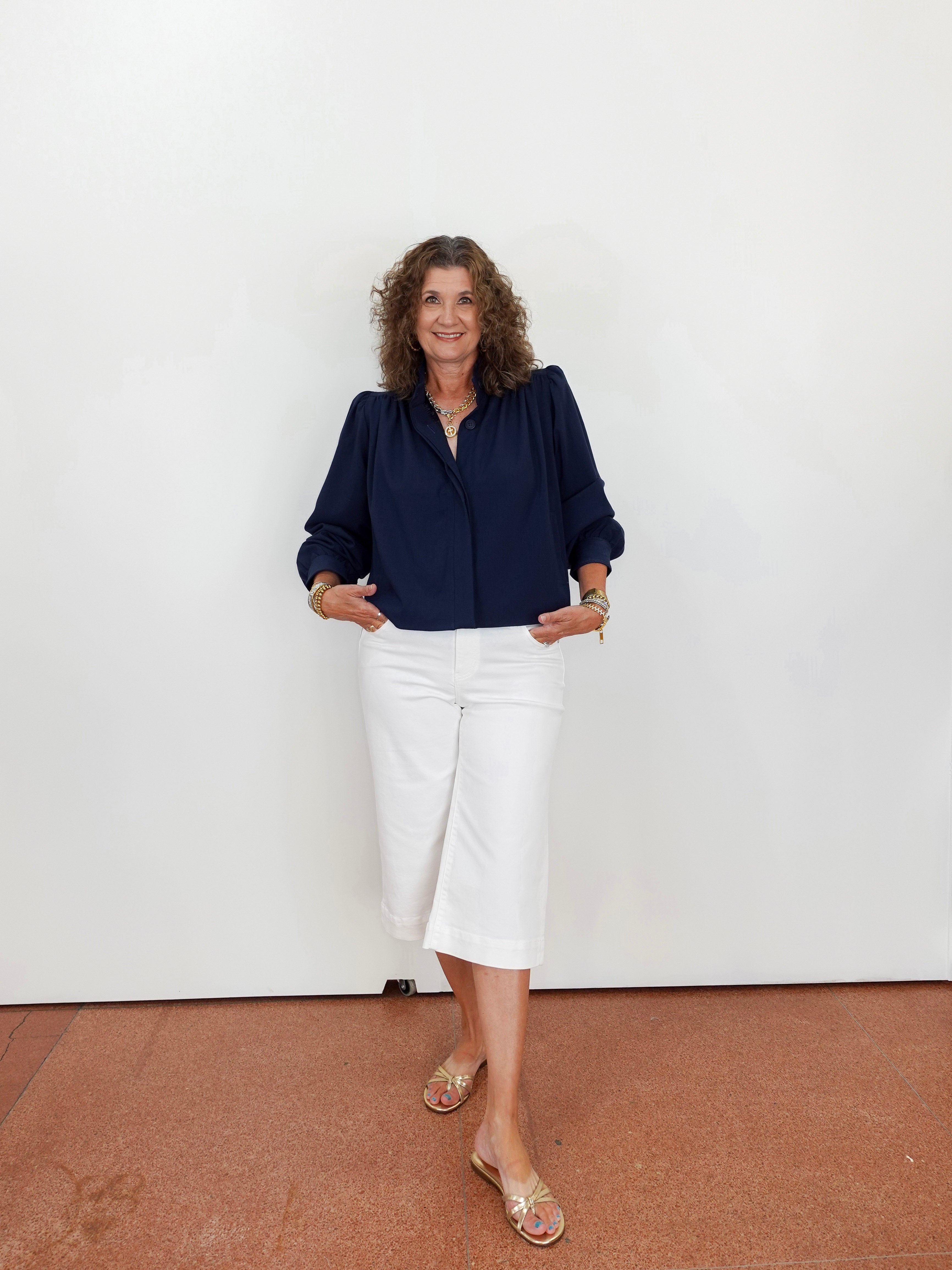 Woman wearing a navy blouse and white pants against a plain background