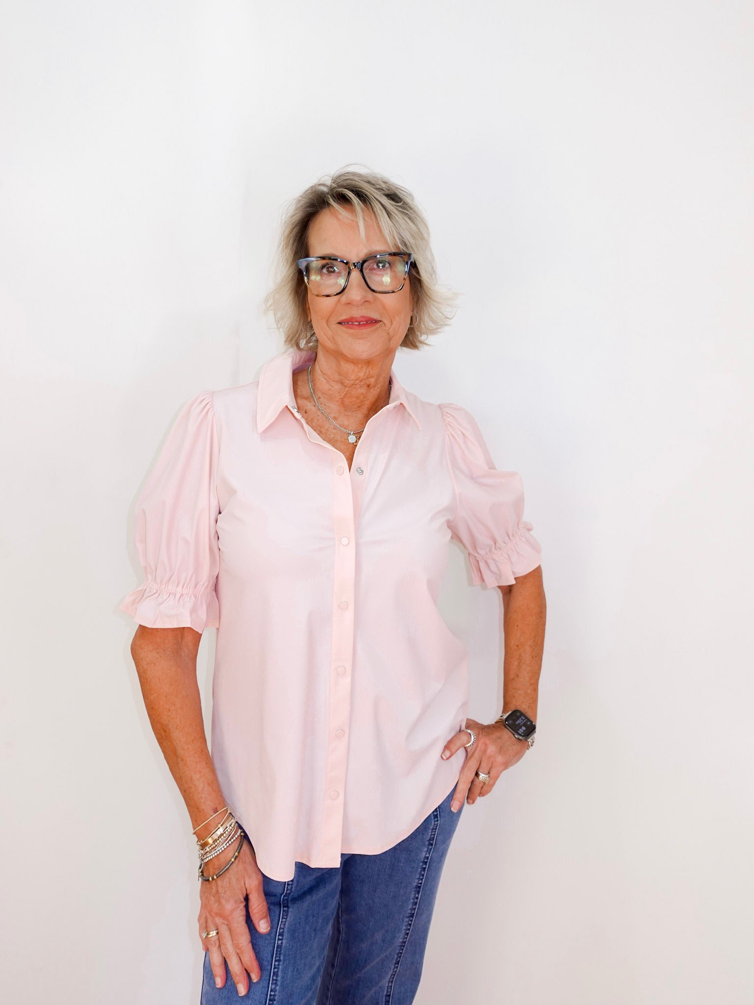 Woman wearing a light pink shirt and blue jeans against a white background
