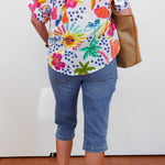 Person wearing a colorful floral shirt and blue jeans with a white background
