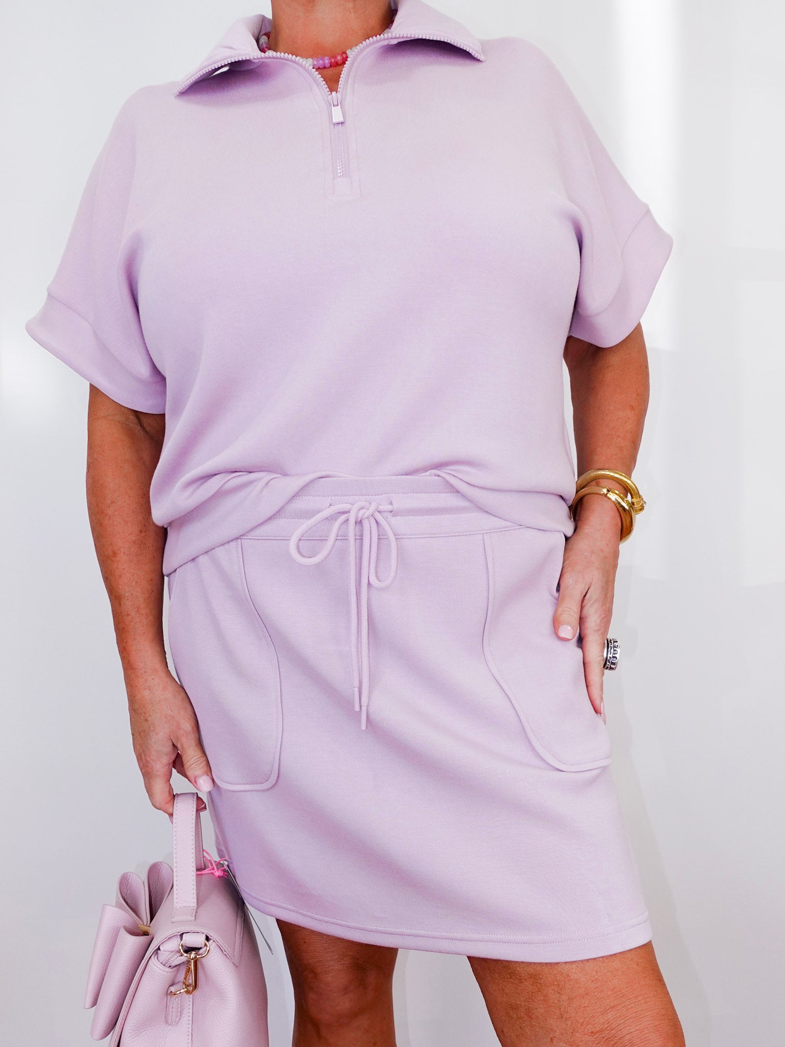 Person wearing a light purple outfit with a matching handbag on a plain background