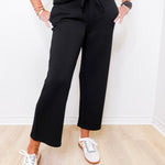 Person wearing black pants and white sneakers in a minimal indoor setting