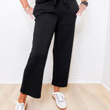 Person wearing black pants and white sneakers in a minimal indoor setting