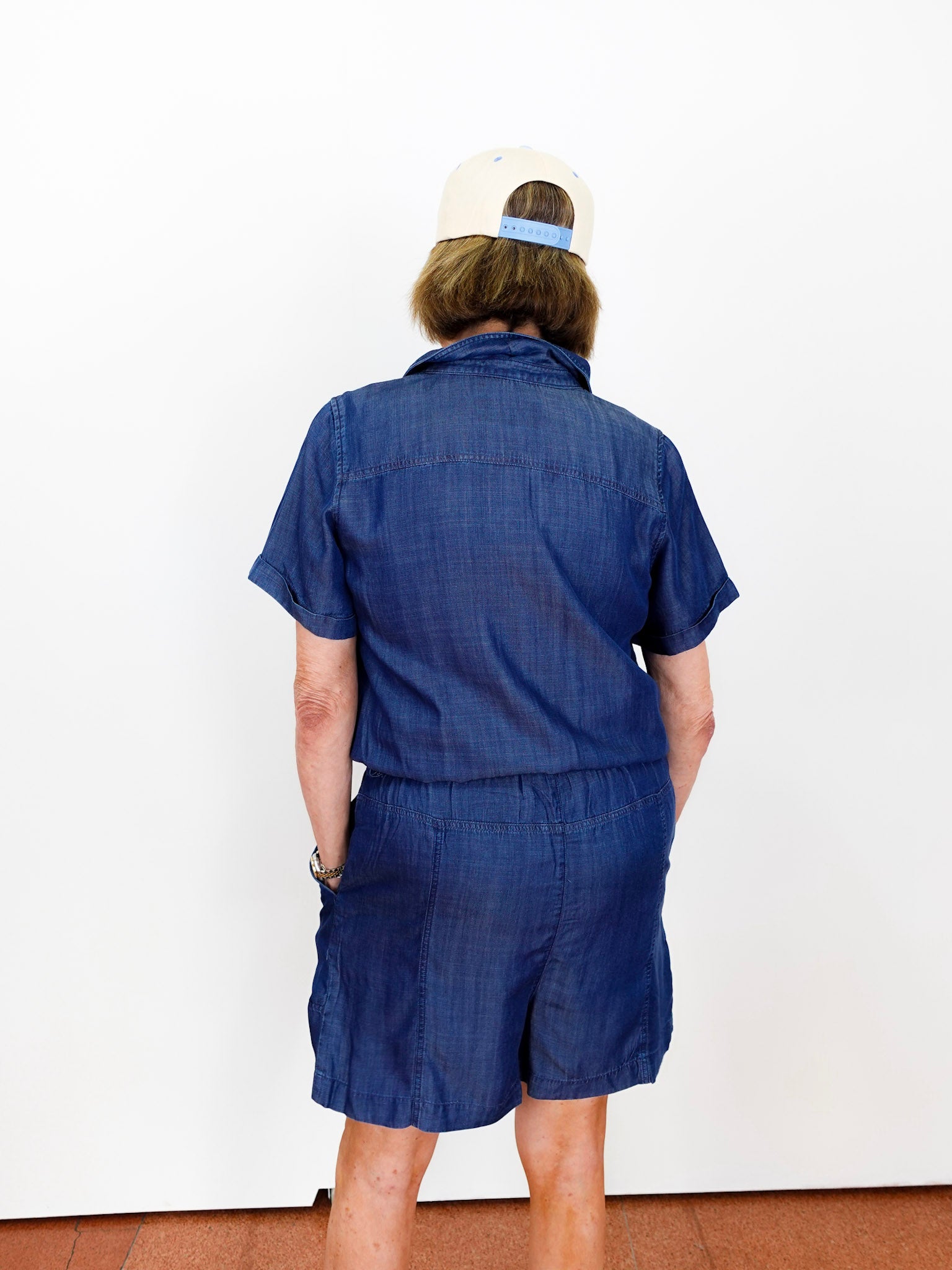 Person wearing a blue outfit with a white cap on a plain background