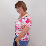 Woman wearing a floral top and jeans against a plain background