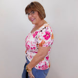 Woman wearing a floral top and jeans against a plain background