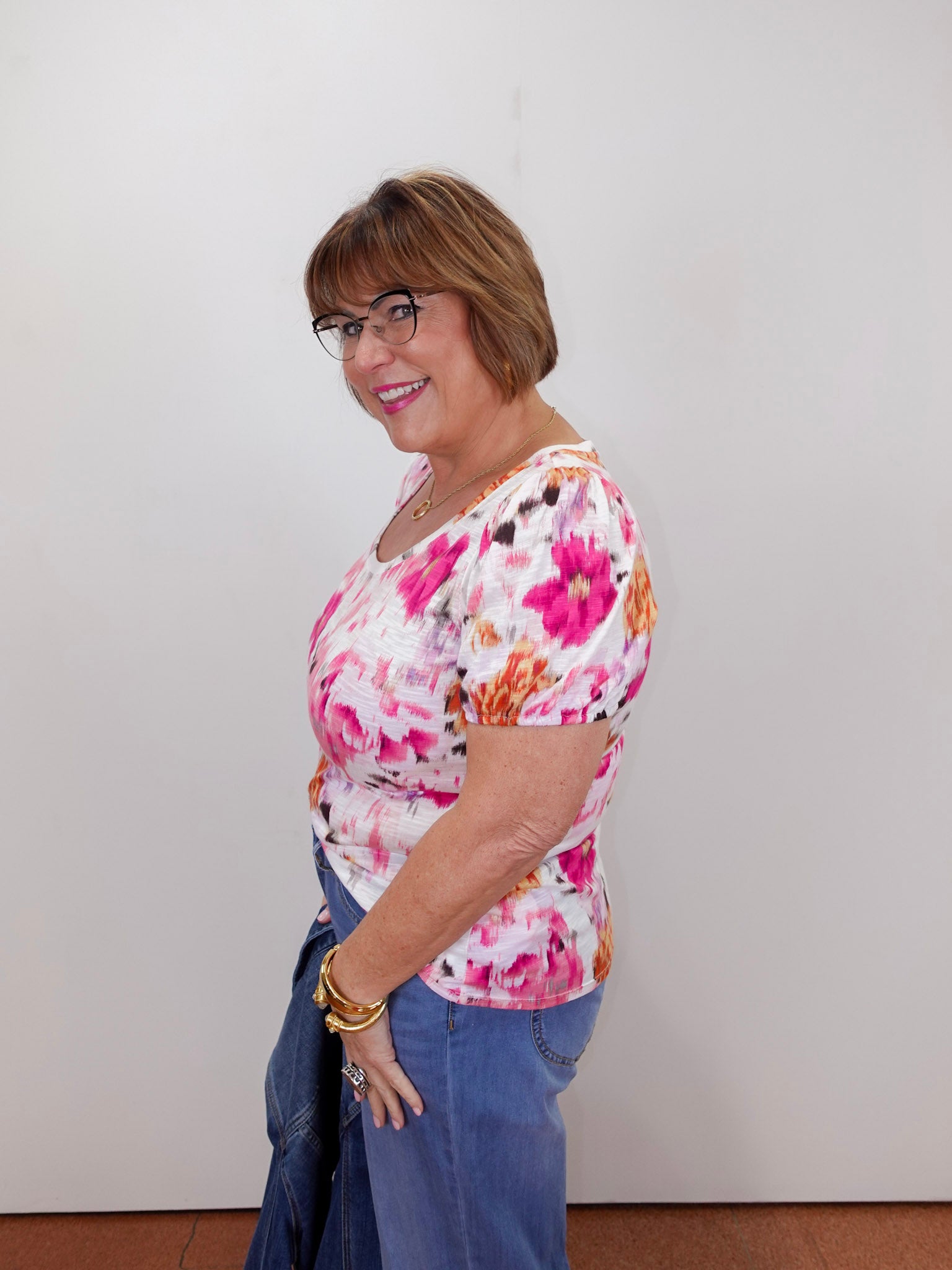 Woman wearing a floral top and jeans against a plain background