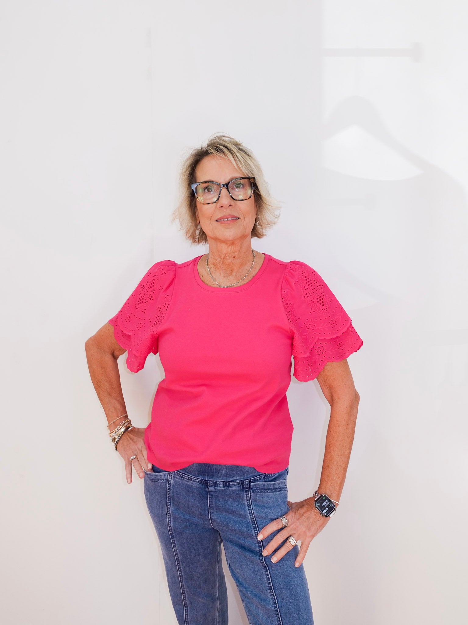 Woman wearing a pink blouse with lace details and blue jeans against a white background