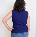 Person wearing a blue sleeveless sweater and jeans against a white background