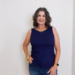 Woman wearing a navy blue sleeveless top and jeans against a white background