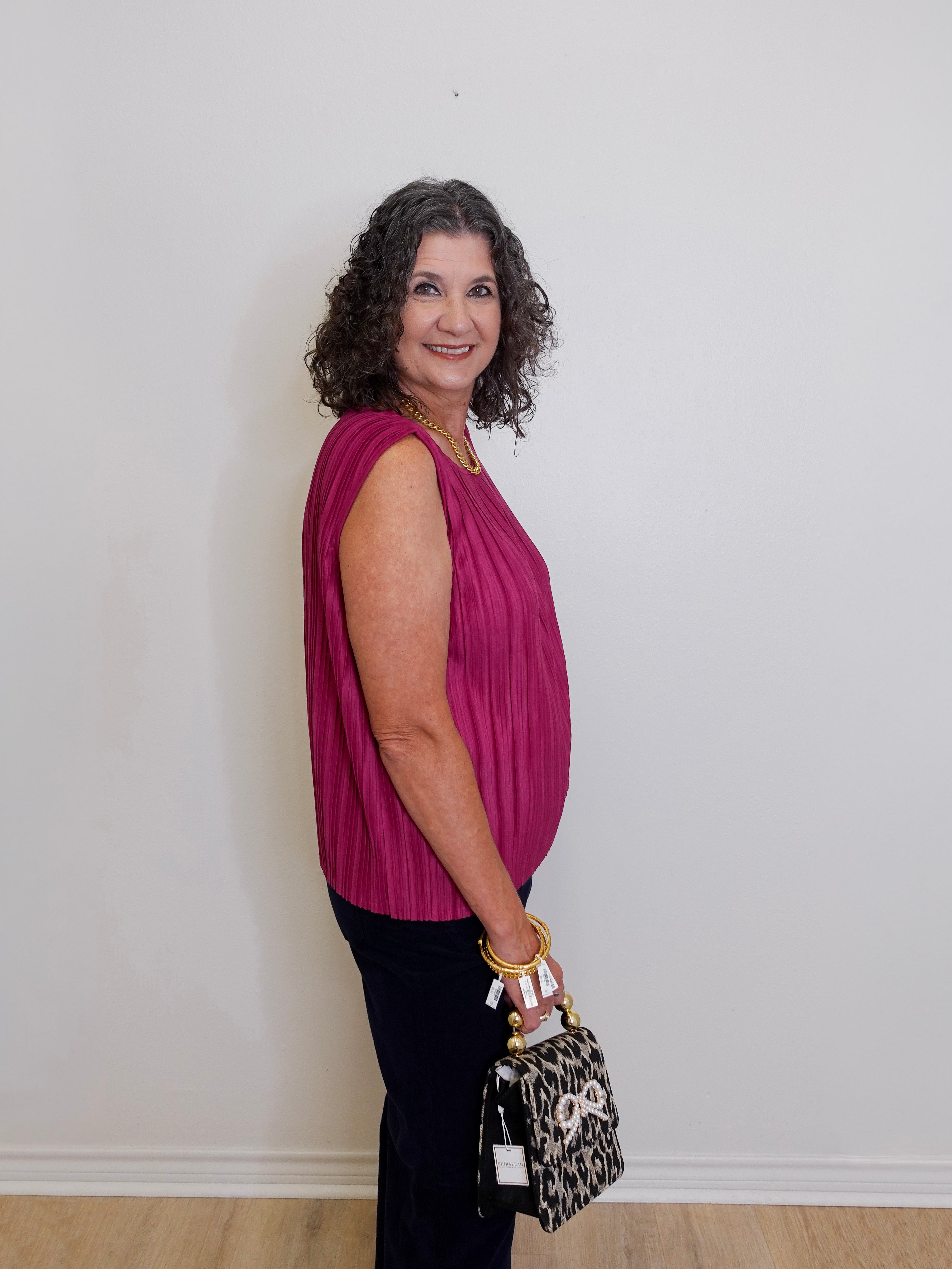 Woman in a pink top holding a leopard print bag against a plain background