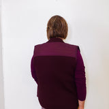 Person wearing a purple vest against a white wall