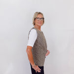 Person wearing a patterned vest over a white shirt with black pants on a plain background