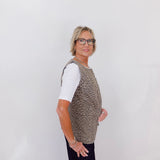 Person wearing a patterned vest over a white shirt with black pants on a plain background