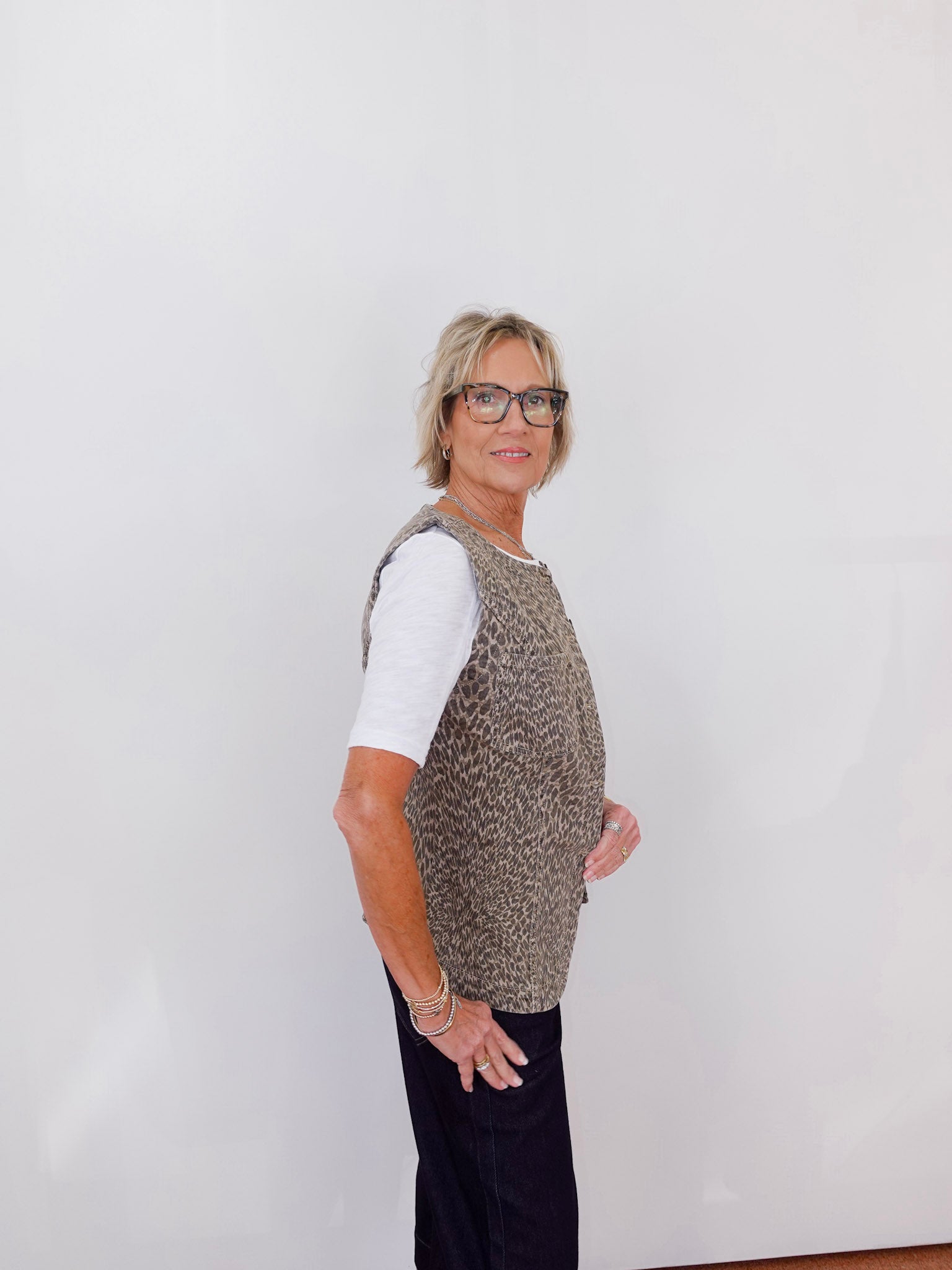 Person wearing a patterned vest over a white shirt with black pants on a plain background